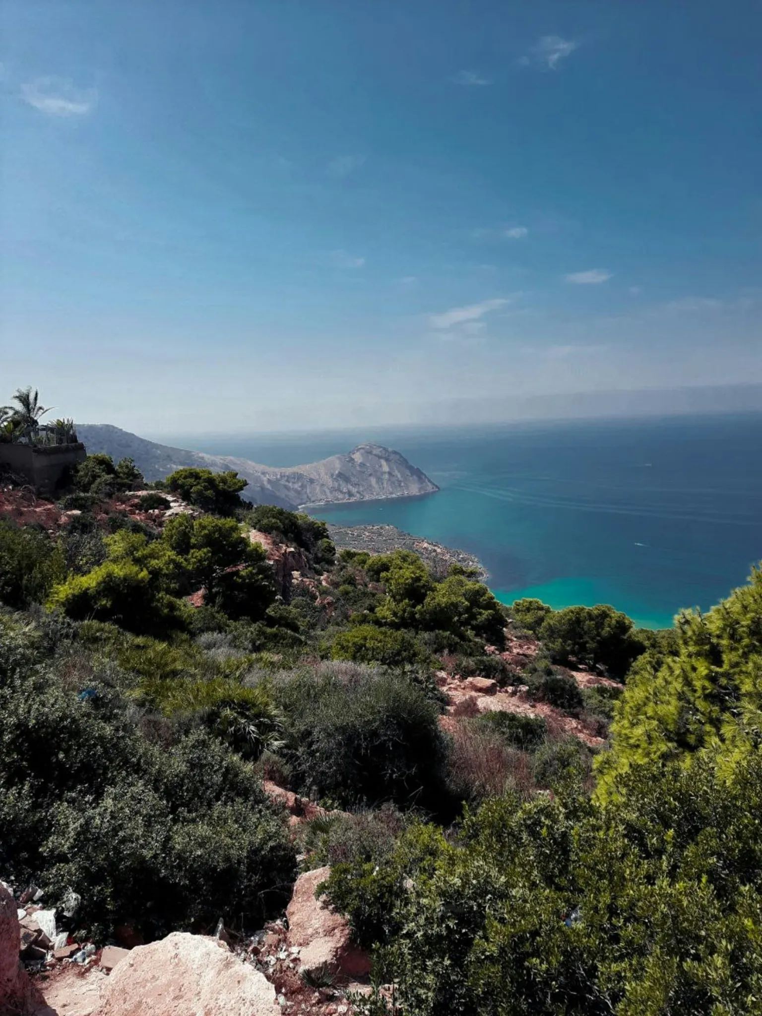 Pente couverte de maquis et de pins qui descend vers une mer turquoise ; au loin, un cap rocheux s’avance dans la Méditerranée