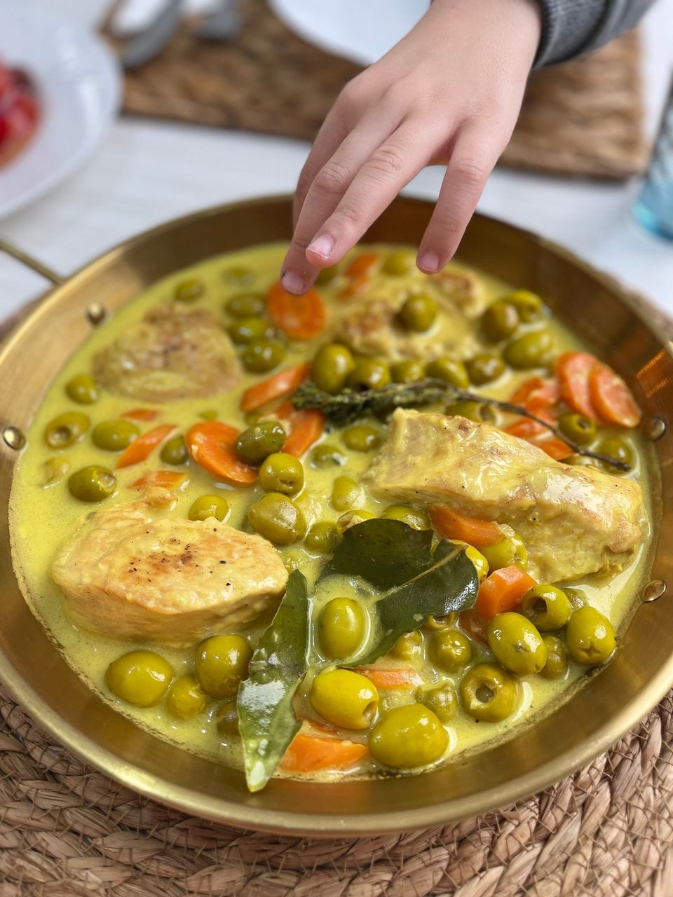 Un plat en laiton rempli d’une sauce jaune où baignent des olives vertes, des rondelles de carotte et des morceaux de viande