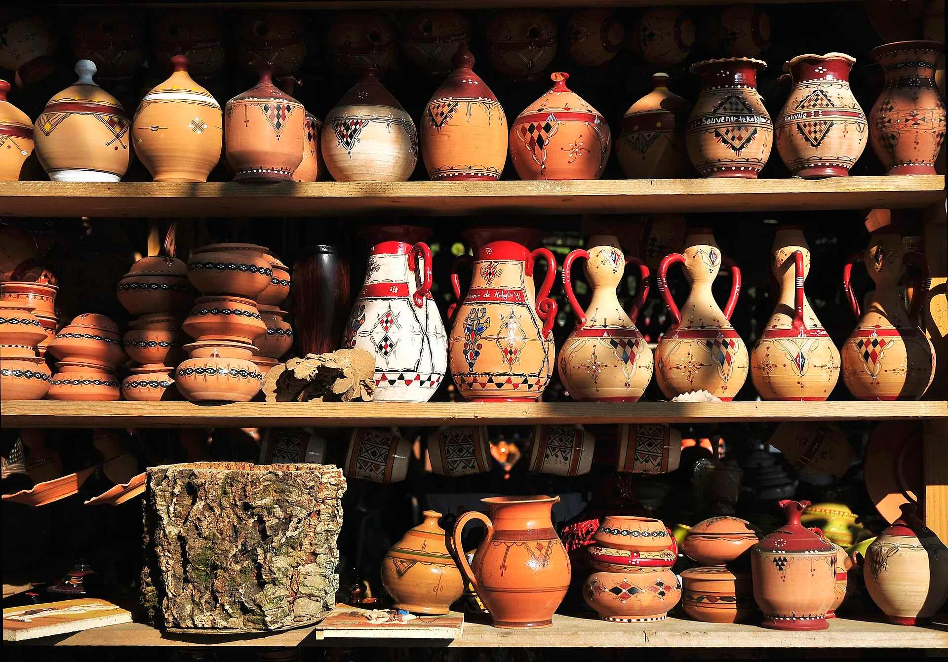 Des étagères chargées de cruches, de jarres et de pots en terre cuite peints de motifs géométriques rouges, noirs et blancs