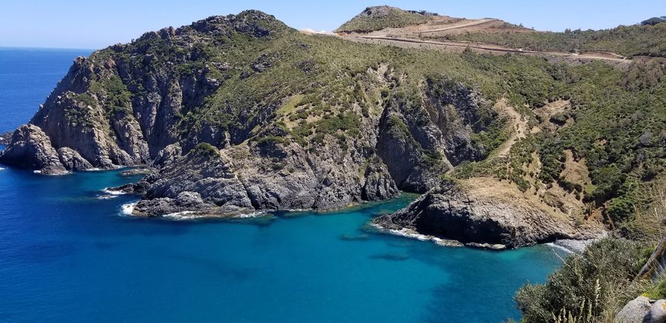 Une crique d’eau turquoise et bleu profond au pied de falaises et de collines couvertes de maquis
