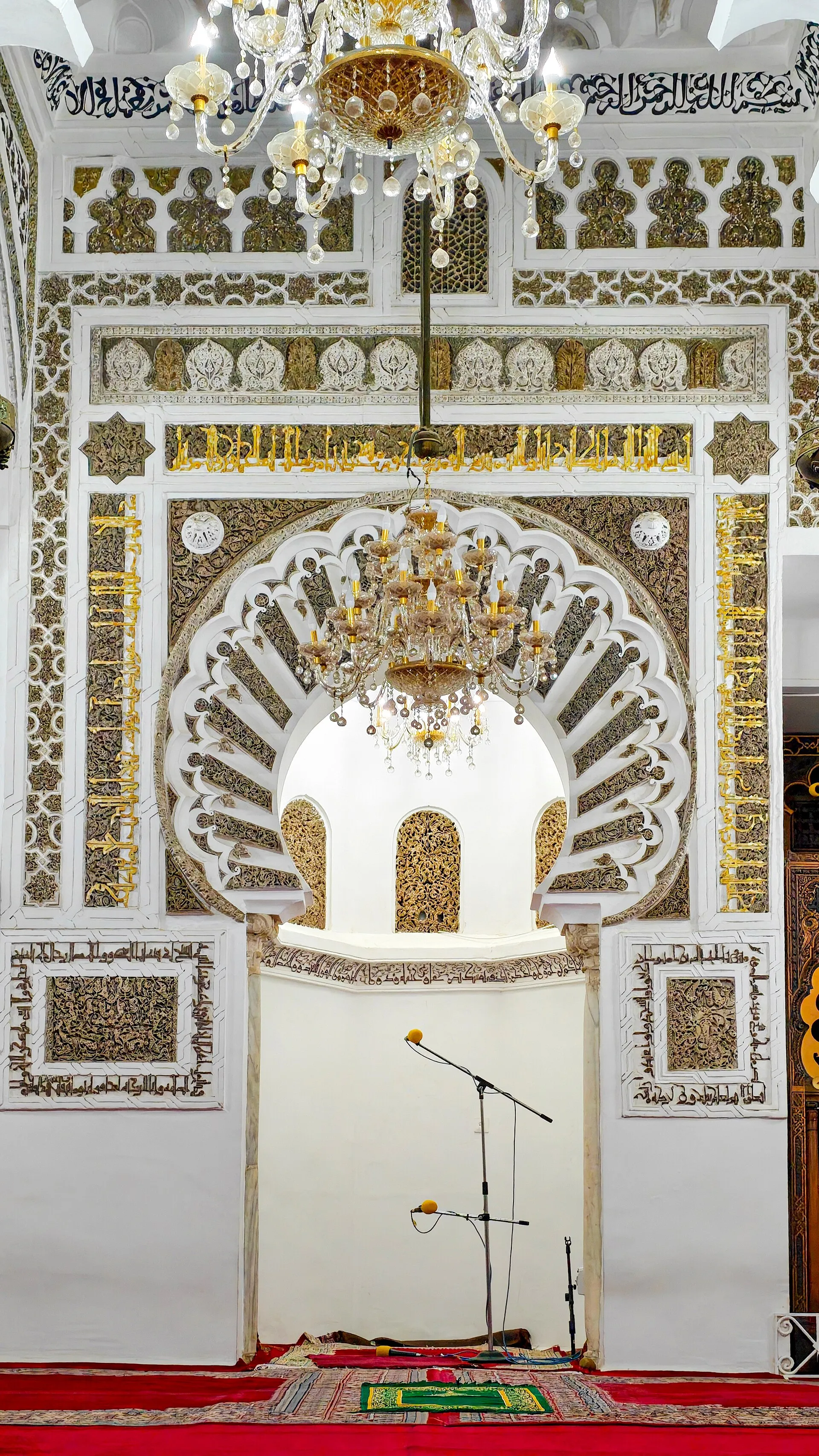 Le mihrab de la Grande Mosquée : une niche encadrée de plâtre blanc finement sculpté, sous des arcs festonnés, avec un lustre suspendu et un tapis rouge au sol
