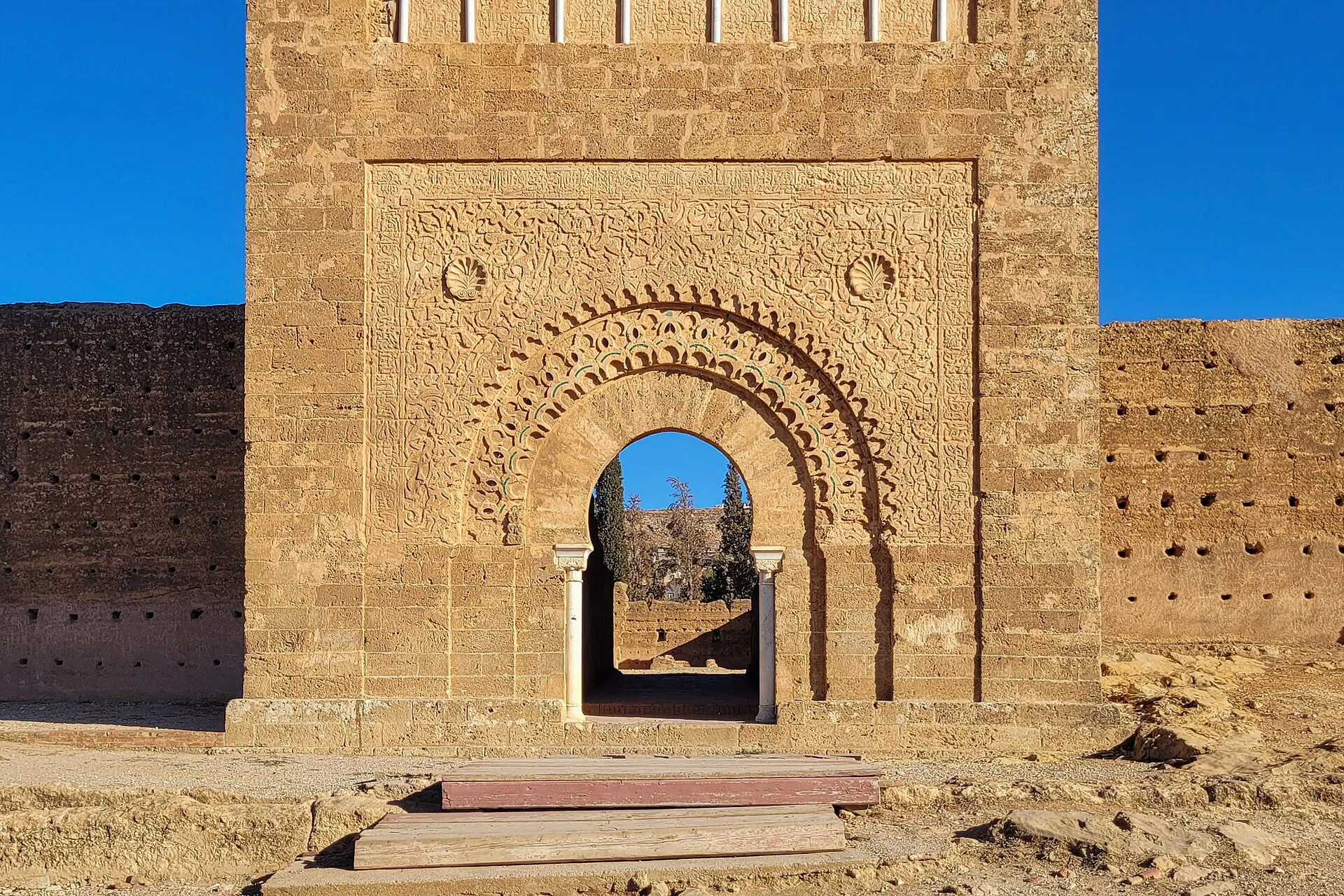 La porte ouverte à la base du minaret de Mansourah : un arc outrepassé à colonnettes, encadré de décors sculptés dans la pierre ocre, entre deux pans de muraille
